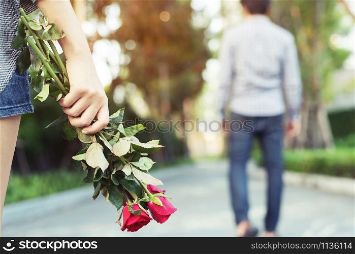 Woman Standing with a Red Rose on Hand Sadness Love in Ending Break up of Relationship Blurred Man Back Side Walking away parting in public park outdoor. Broken Heart in Valentine day Concept.