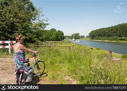woman standing with bike looking at the boats going by on the river in Holland