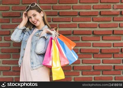 woman standing with bright shopping bags back brick wall