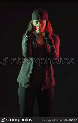 Woman standing with her fists balled up in front of a dark background. 