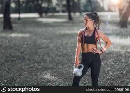 Woman Standing with Kettlebell and Elastic Band Outdoors after training