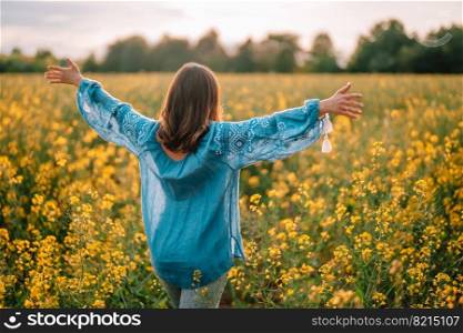Woman standing with open arms in yellow canola field. Happy free lady in blue embroidered blouse. Alternative energy sources, oil production, biodiesel manufacturing, honey plant. High quality photo. Woman standing with open arms in yellow canola field. Happy free lady in blue embroidered blouse. Alternative energy sources, oil production, biodiesel manufacturing, honey plant.
