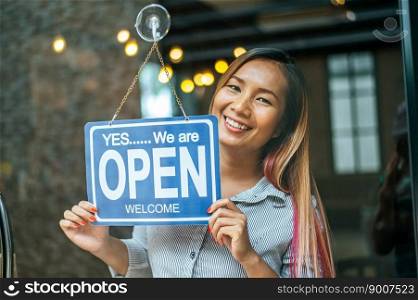 woman stands and opens a wide sign through the shop window and smile.