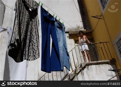 Woman stands on steps with washing in courtyard, Lisbon, Portugal