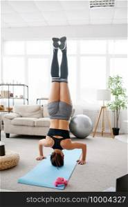 Woman stands upside down, online yoga training at the laptop. Female person in sportswear, internet sport workout, room interior on background. Woman stands upside down, online yoga training
