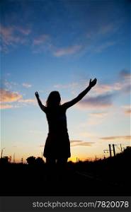 Woman staying with raised hands at the sunset time