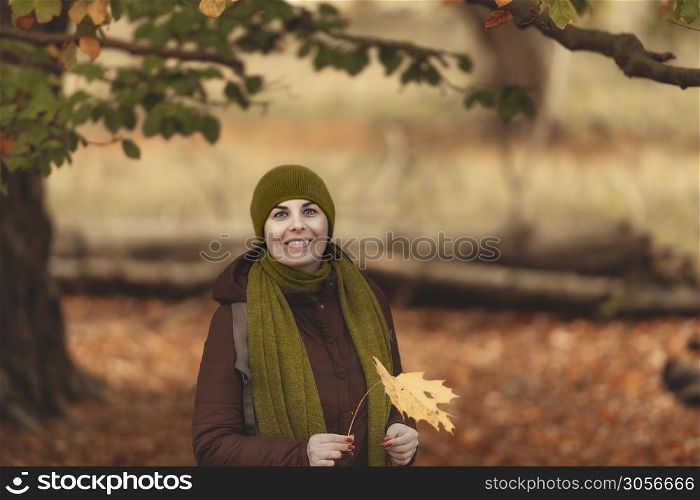 Woman stays in the park and holds yellow leaf