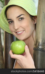 Woman stood by wooden poles holding a green apple