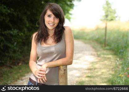 Woman stood outdoors resting against wooded pole