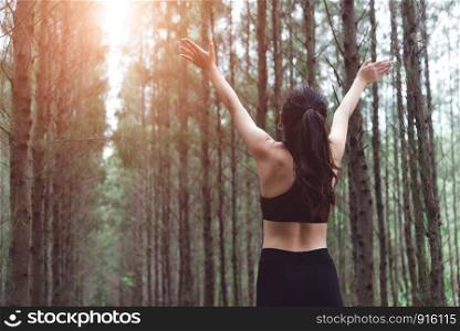Woman stretching arms and breathing fresh air in middle of pinewood forest while exercising. Workouts and Lifestyles concept. Happy life and Healthcare theme. Nature and Outdoors theme. Back view