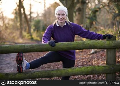 Woman Stretching On Run Through Winter Woodland