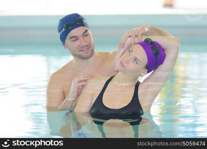 woman stretching with trainner inside a swimming pool