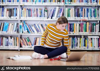 Woman student taking notes from a book at library. Young woman sitting and doing assignments in college library.