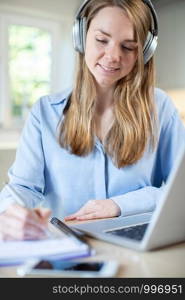 Woman Studying At Home Using Laptop And Wearing Headphones