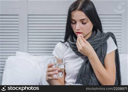 woman suffering from cold holding glass water taking medicine