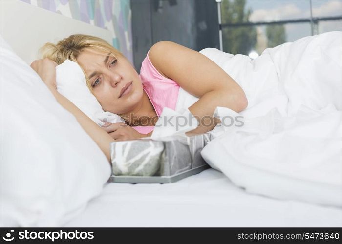 Woman suffering from cold lying with tissue box on bed