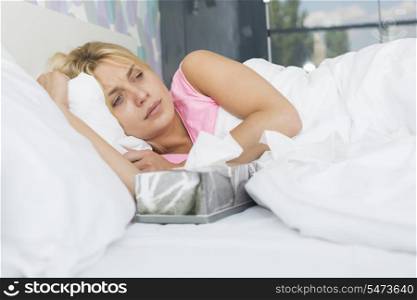 Woman suffering from cold lying with tissue box on bed