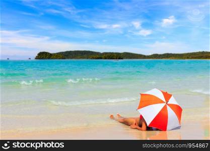 Woman sunbathing with orange umbrellas on the beach.