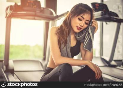 Woman sweats by towel during rest in fitness gym with fitness running equipment. Beauty and relax concept. Gym and fitness training theme