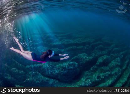 Woman swimming underwater in the Mediterranean. Rays of light entering the water from the left. . Girl snorkelling underwater in the Mediterranena sea