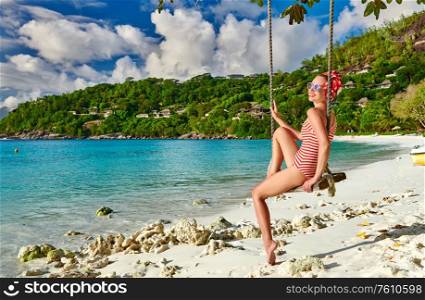 Woman swinging at tropical beach, Petite Anse, Mahe, Seychelles.