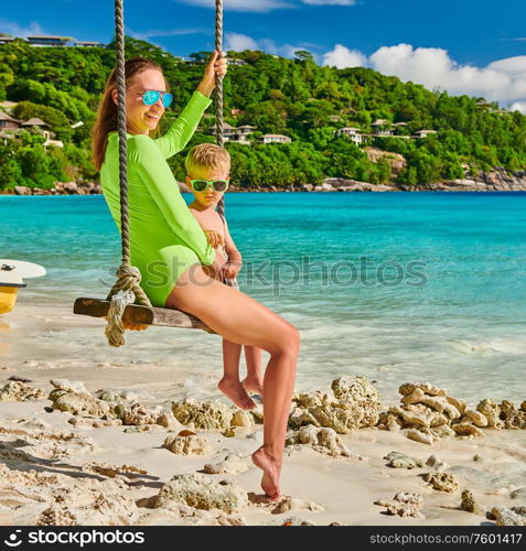 Woman swinging with three year old son at tropical beach, Petite Anse, Mahe, Seychelles.