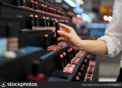 Woman takes lipstick from shelf in cosmetics store. Buyer at the showcase in luxury beauty shop salon, female customer in fashion market. Woman takes lipstick from shelf in cosmetics store