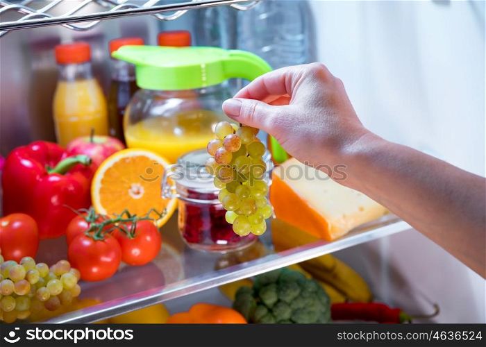Woman takes the bunch of grapes from the open refrigerator. Healthy food.
