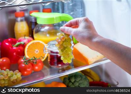 Woman takes the bunch of grapes from the open refrigerator. Healthy food.