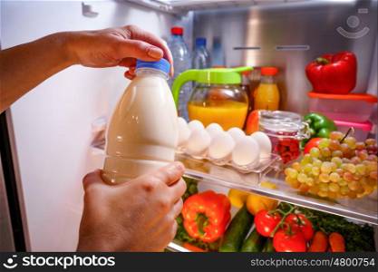 Woman takes the milk from the open refrigerator