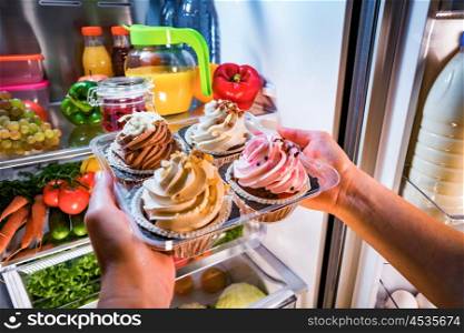 Woman takes the sweet cake from the open refrigerator