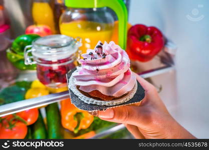 Woman takes the sweet cake from the open refrigerator