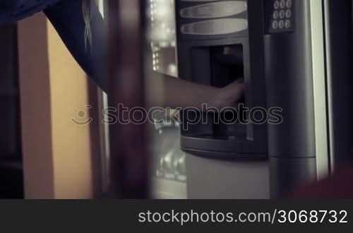 Woman taking a plastic cup from coffee vending machine and pushing some buttons