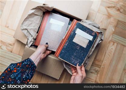 Woman taking books out of cardboox. Unpacking parcel. Female hands holding books