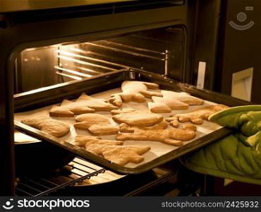 Woman taking out of the gingerbread cookies from the oven
