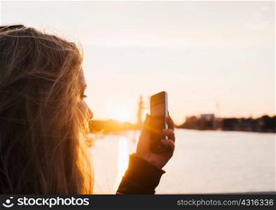 Woman taking photograph at sunset, Spree River, Berlin, Germany