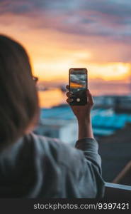 Woman taking photos of the sea from the balcony with a smartphone