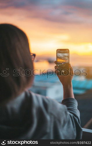 Woman taking photos of the sea from the balcony with a smartphone