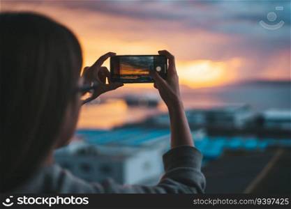 Woman taking photos of the sea from the balcony with a smartphone