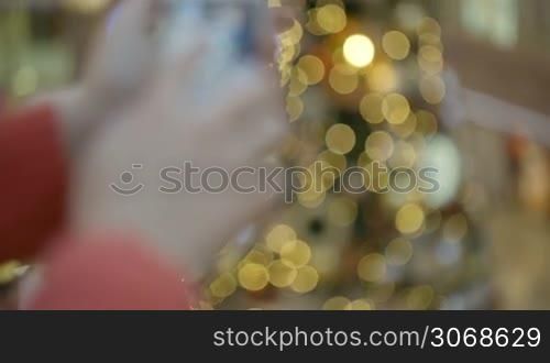 Woman taking pictures of beautiful Christmas tree in shopping centre. Zooming in on the object during process.