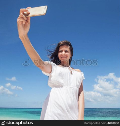Woman taking selfie on beach. Smiling young woman taking selfie with smartphone on beach