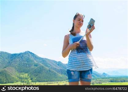 Woman taking selfie on mobile phone. Woman taking selfie on mobile phone with stick. Vacation in the mountain