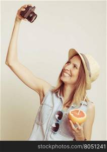 Woman taking selfie self picture with camera.. Happy tourist woman in straw hat taking selfie self picture with camera while holding grapefruit fruit in hand. Summer vacation holiday.