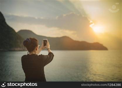 woman taking sun rise photograph by smart phone at sea side