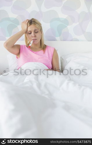 Woman taking temperature with thermometer while suffering from headache