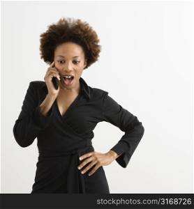Woman talking on cellphone looking shocked against white background.