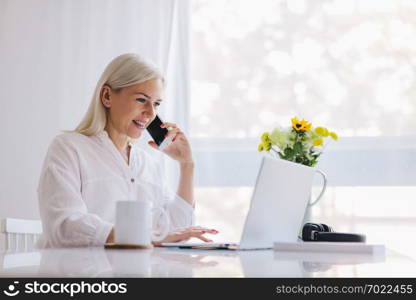 Woman talking on the phone, using laptop. Working from home, freelancing, online job.. Woman talking on the phone, using laptop.