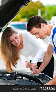 Woman talking to a car mechanic in a parking area, both are standing next to the car