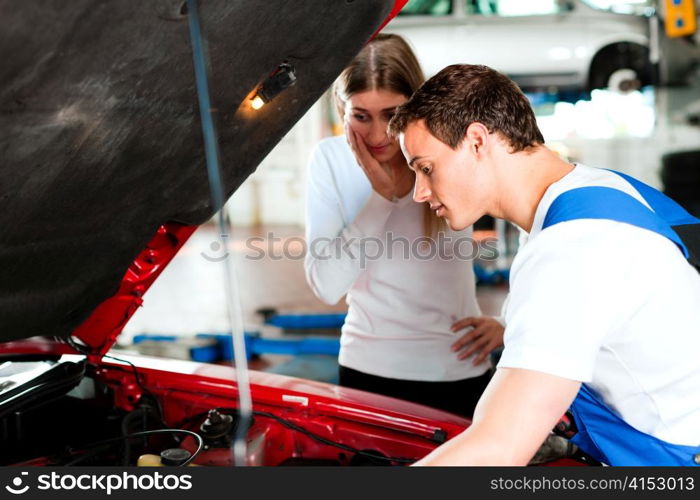 Woman talking to a car mechanic in his repair shop, both are standing next to the car