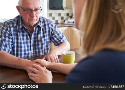 Woman Talking With Unhappy Senior Man Sitting In Kitchen At Home                             
